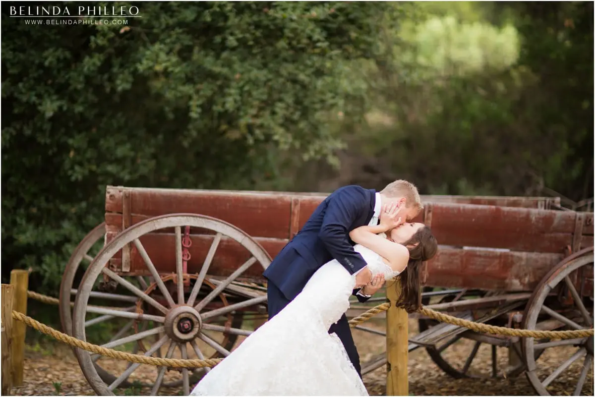 Bride and groom kiss near an antique wagon at Temecula Creek Inn wedding. Photos by Belinda Philleo