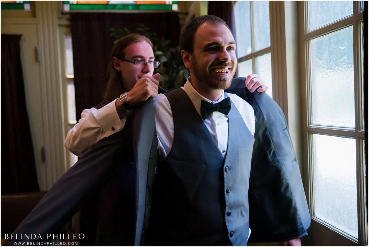 Groom's brother helps him get dressed in his grey tux for his El Dorado Park Golf Course Wedding