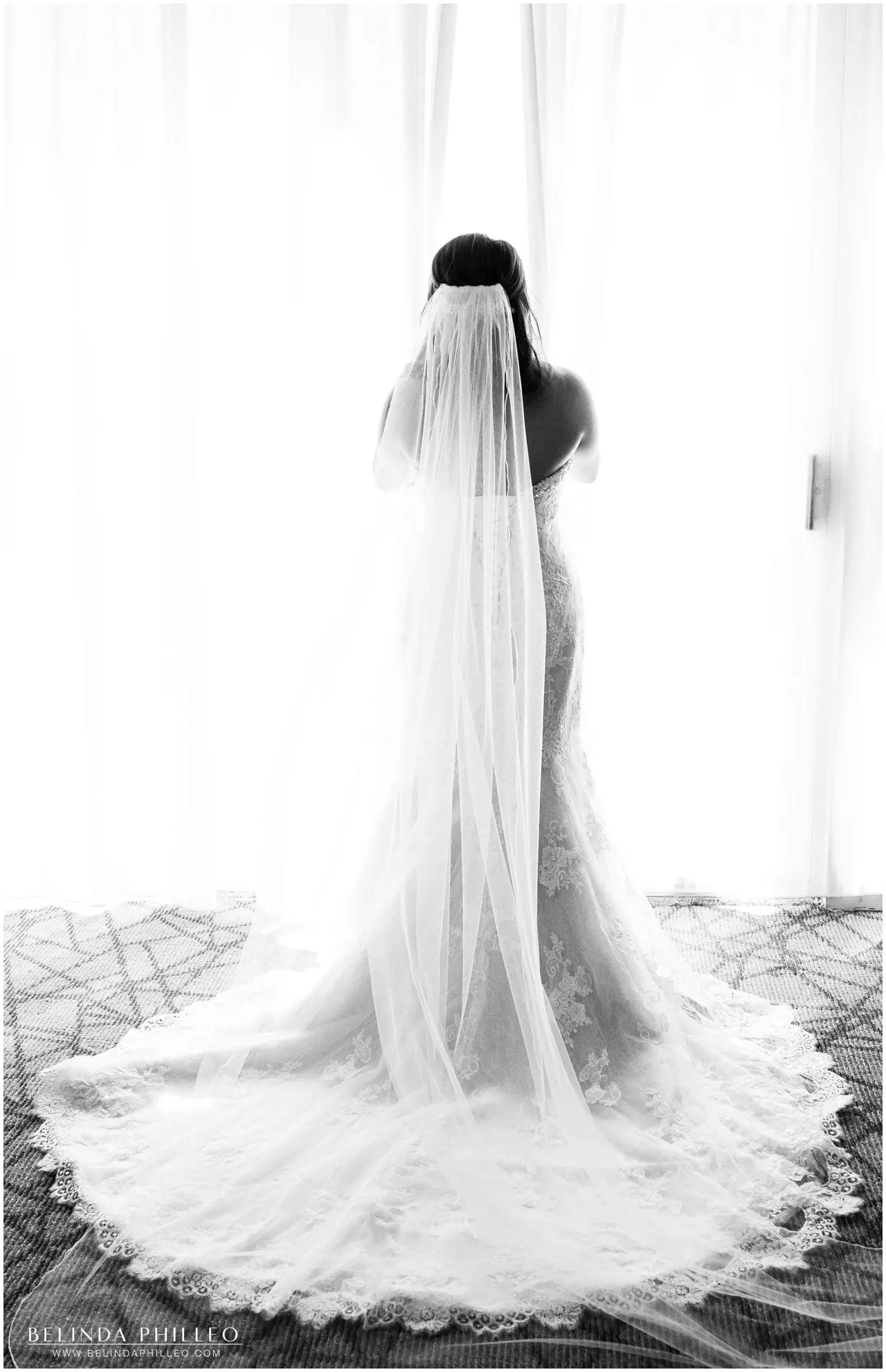 bride wearing her maggie sottero gown looks out the window before the ceremony