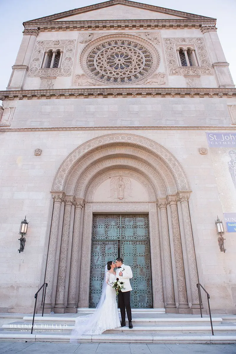 Bride and groom share a kiss on the front steps of St John's Cathedral in Los Angeles, CA. Photography by Belinda Philleo