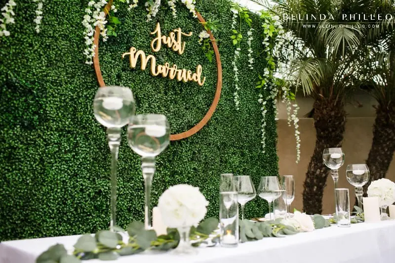 Sweetheart table for backyard wedding with eucalyptus, green plant wall, candles, and wooden just married sign