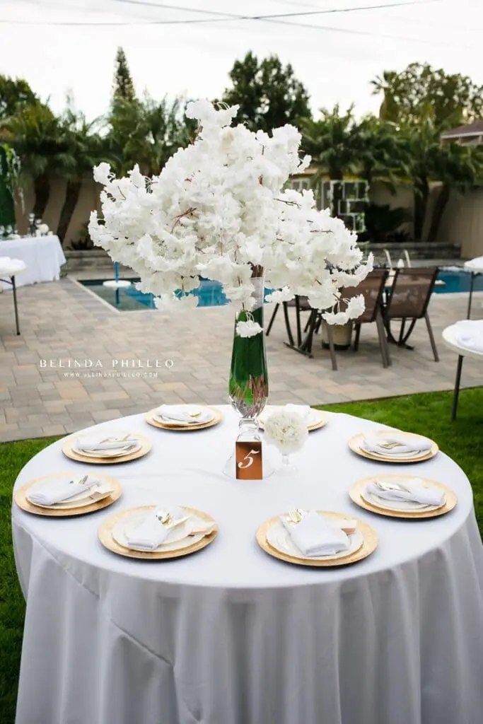 Backyard wedding reception tables with gold dinnerware and white floral centerpieces