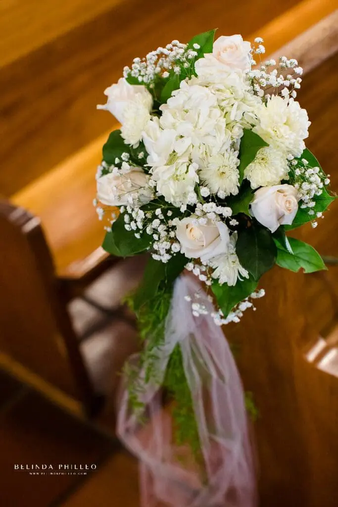 White roses, jasmine, and babies breath decorate church pew for wedding in Orange County, California. Photography by Belinda Philleo