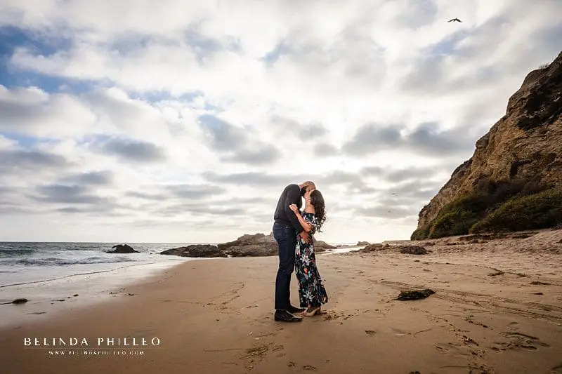 couple shares a kiss under an epic cloudy sky during Crystal Cove engagement photos session by Belinda Philleo