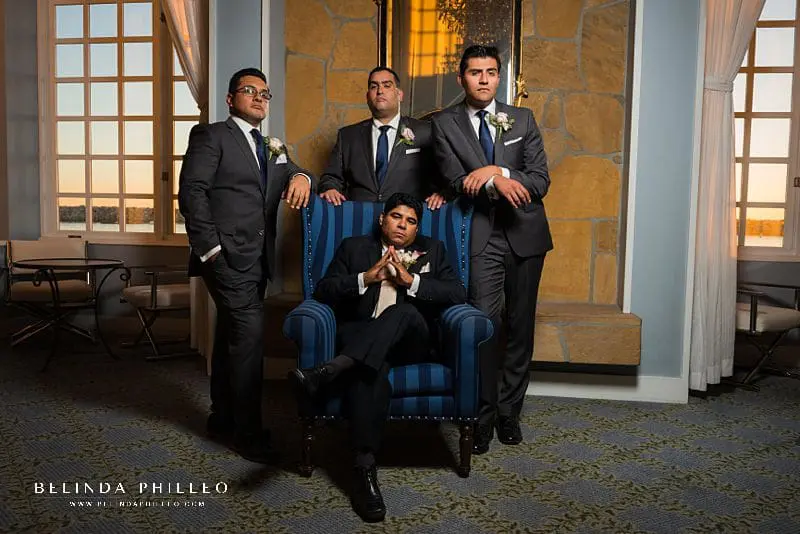 Posing tips for men shared by Southern California wedding photographer Belinda Philleo. A groom sits in a chair while three groomsmen pose looking tough behind him.