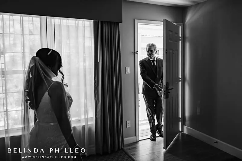 Get great wedding photos with parents by planning a parent first look. Bride's father opens the door to see his daughter as a bride for the first time.