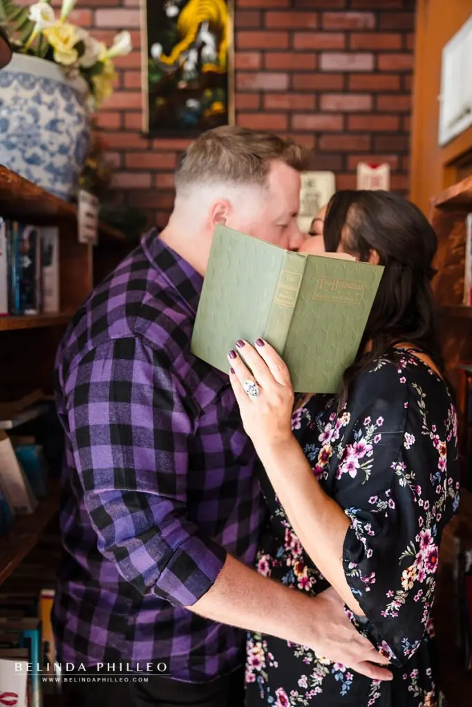 An engaged couple share a kiss behind a book, The Betrothed