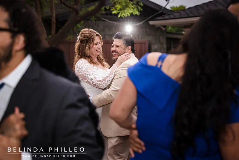 A shot through the crowd on a dance floor shows a bride and groom laughing and lost in eachother's eyes