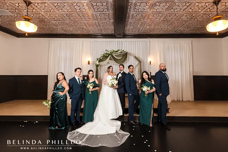 Bridesmaids and groomsmen are standing in altnernating poses around the newlyweds