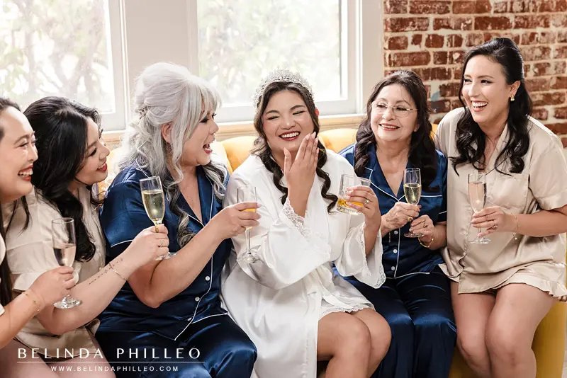 Bride and her bridesmaids laughing as they toast with a glass of champagne
