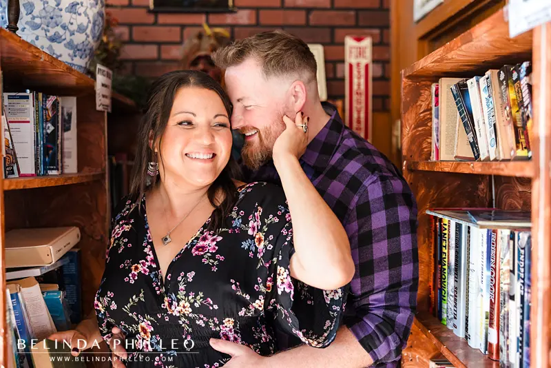 An engaged couple flirt as they browse books in a coffee shop library