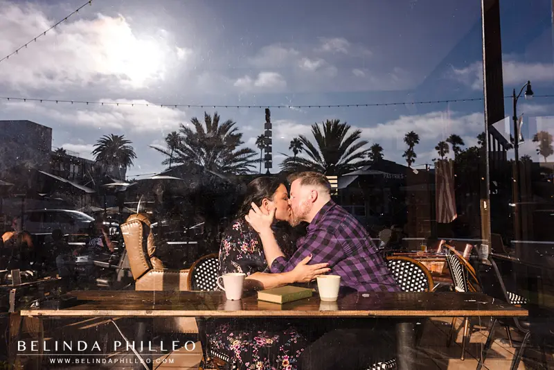Engaged couple shares a kiss near the window in their favorite coffee shop
