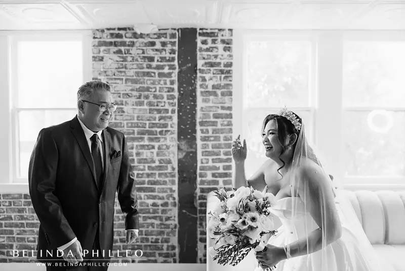 The bride wipes a tear away from her eyes and laughs as she reveals her bridal look to her father before the wedding