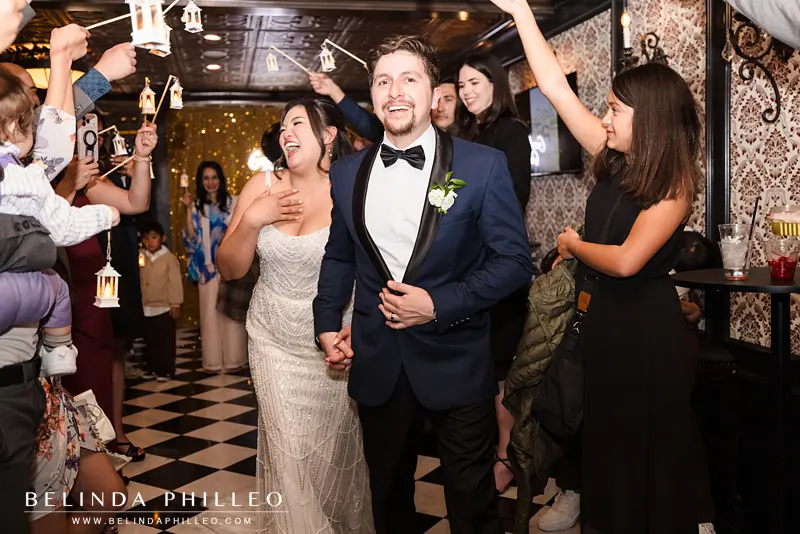 Bride and groom make a grand exit by walking through a cheering crowd with miniature lanterns