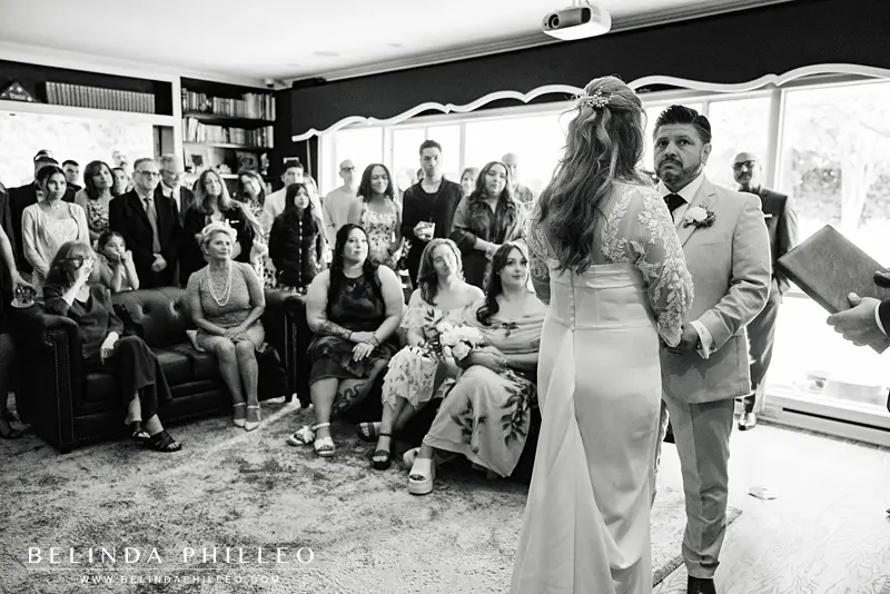 Black and white image of a couple getting married in their living room as a small crowd looks on