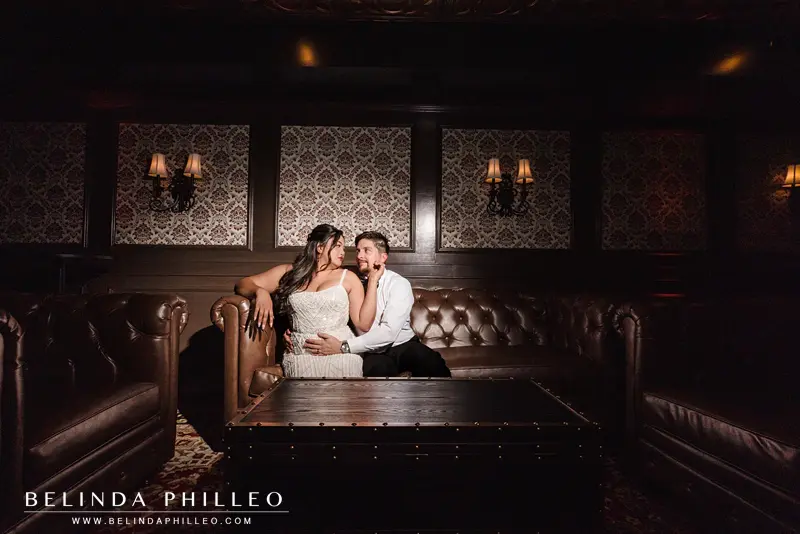 A dark portrait of the bride and groom sharing a romantic moment while seated on a leather couch