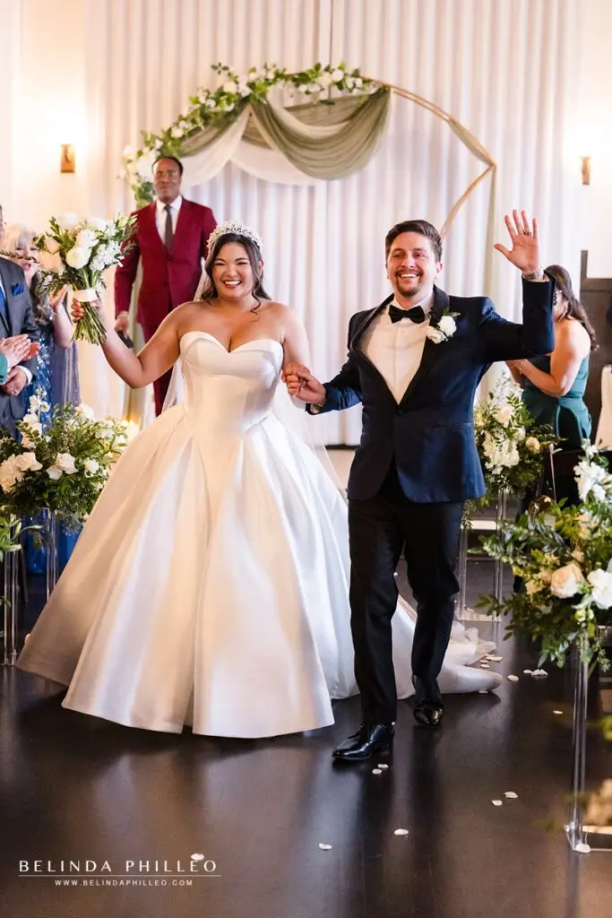 Bride and groom wave to their guests as they make their way back down the aisle