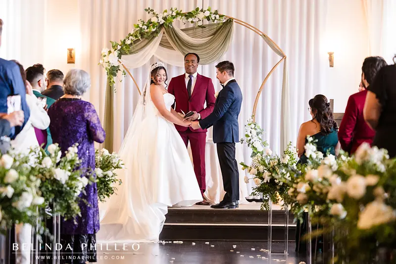 Bride and groom hold hands during their wedding ceremony and guests look on