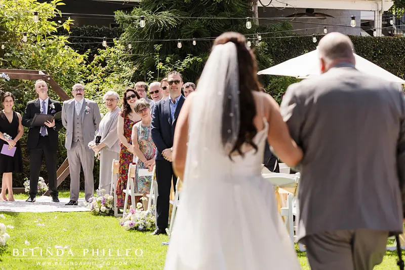 Groom watching as his bride is walked down the aisle by her father during their ceremony in Orange, CA