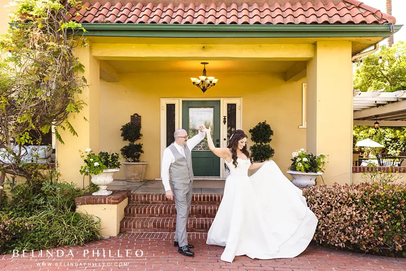 Groom twirls his bride in front of the steps at The French Estate in Orange, CA
