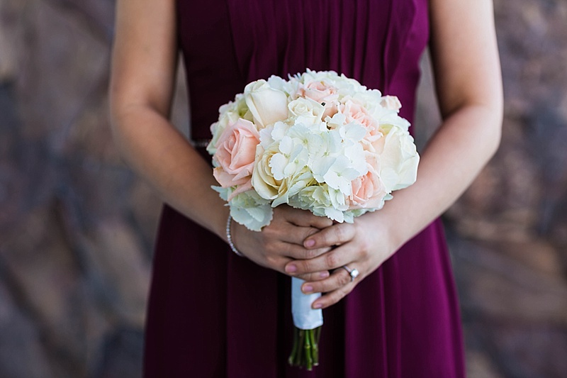 bridesmaid in burgundy gown shows off her bouquet of white hydrangeas and white and pink roses