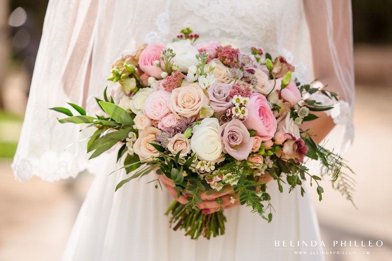 Spring florals in a bridal bouquet with pink and purple roses and white ranunculus