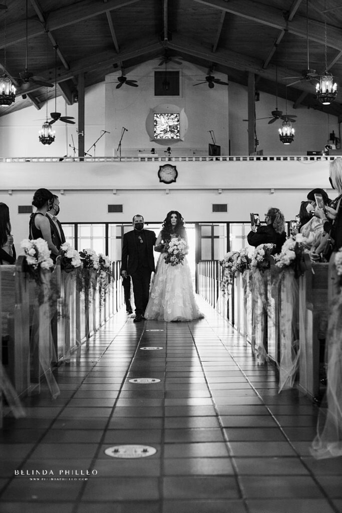 Black and white image of bride being escorted down the aisle by her father during wedding in Westminster, California. Photography by Belinda Philleo