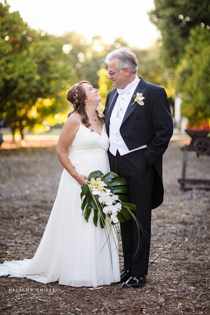 Bride and groom smile coyly at each other in the orange grove at their Heritage Museum of Orange County wedding. 