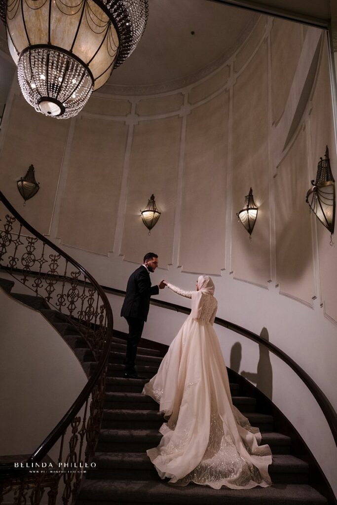 Groom takes his bride's hand on elegant staircase at The Brandview Ballroom in Glendale, CA. Photo by Belinda Philleo