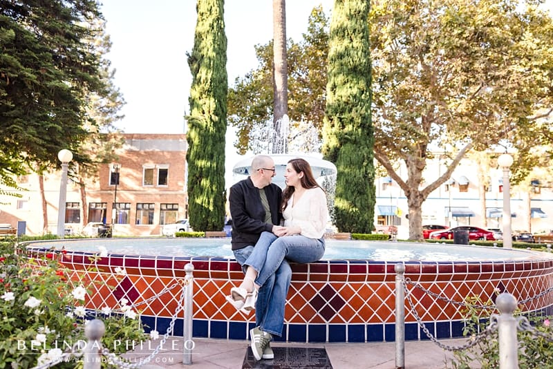Engaged couple sitting on the fountain in Old Towne Orange Circle during a romantic engagement session.